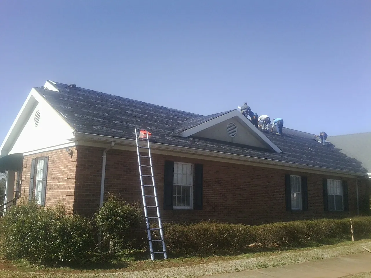 Crew tearing shingles off a brick ranch roof with a ladder set — Metal Roof Repair work by our crew in Rathdrum