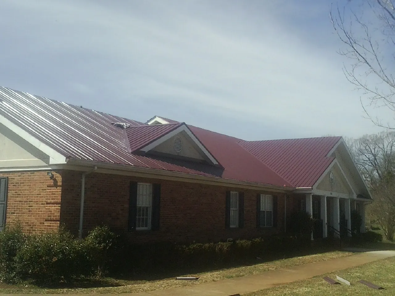 Red metal roof with gabled entries on a long brick building, from a Hail Damage Roof Repair job in Rathdrum