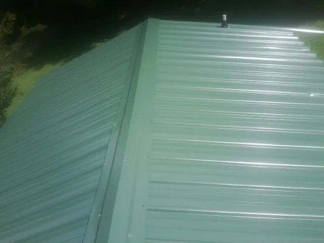 New green metal panels meeting at the ridge of a roof — Flat Roof Repair work by our crew in Rathdrum