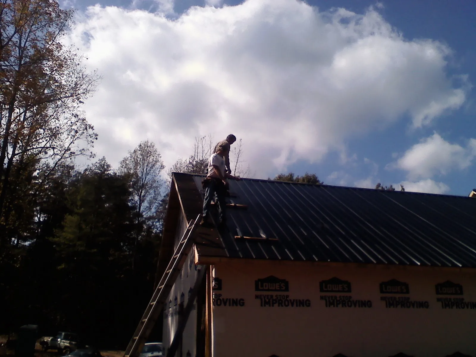 Roofer fastening dark metal panels high against a cloudy sky, from a Roof Inspection job in Rathdrum